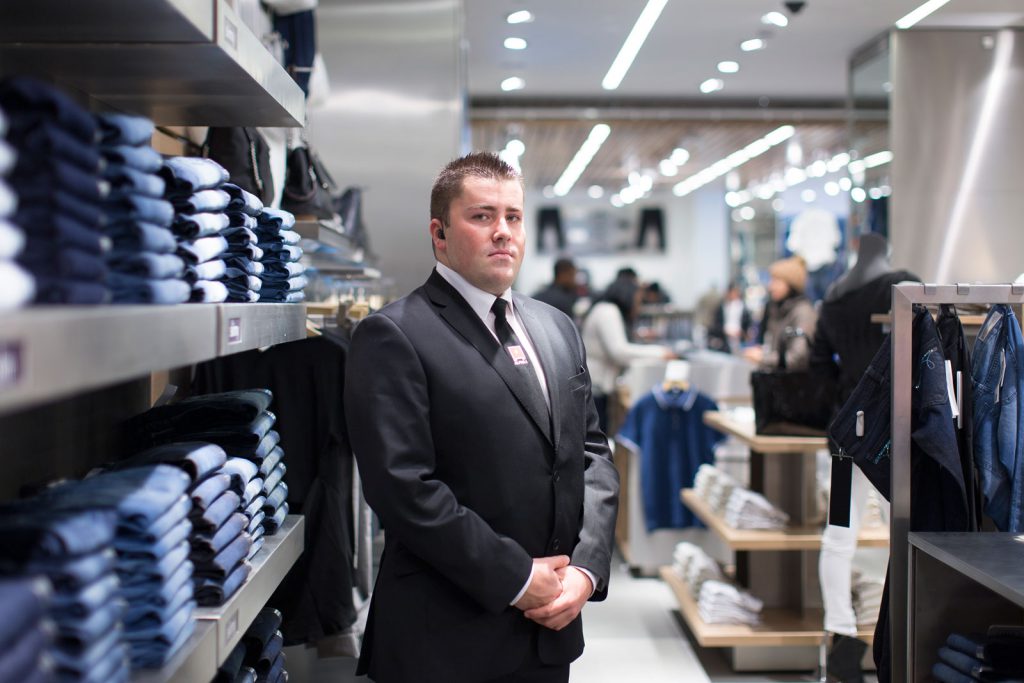 A security guard inspecting a retail store with surveillance cameras and monitoring equipment.